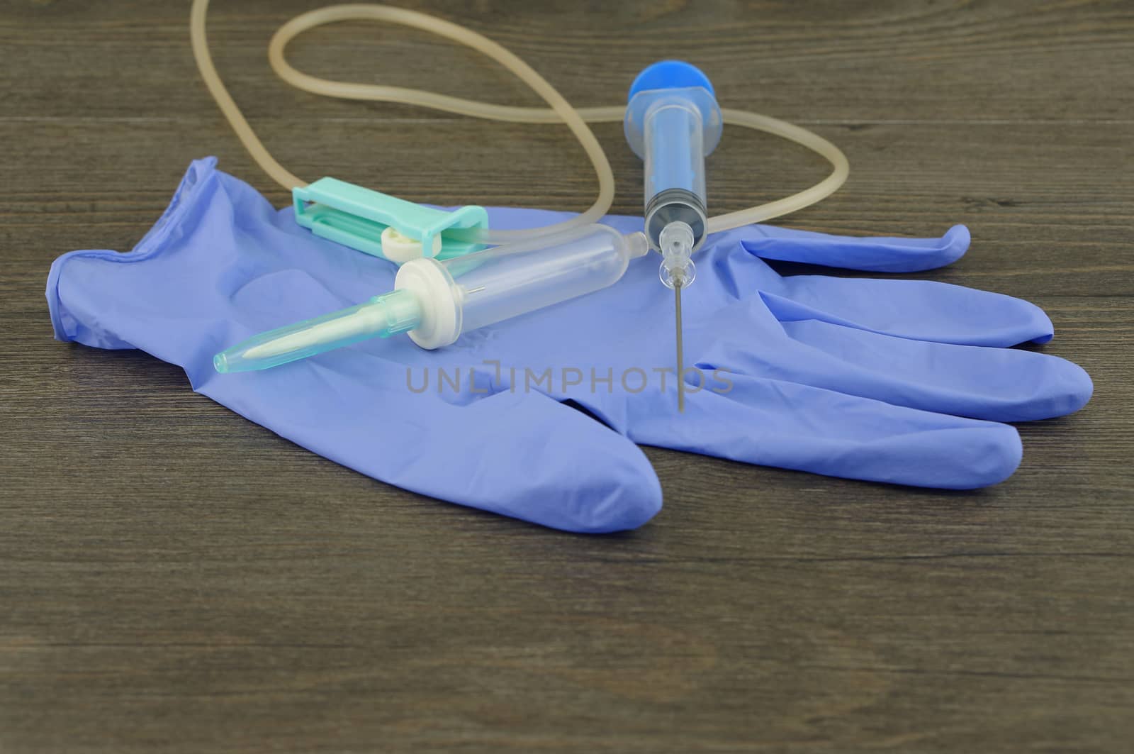 Disposable infusion set, syringe and glove placed on wooden table.                               