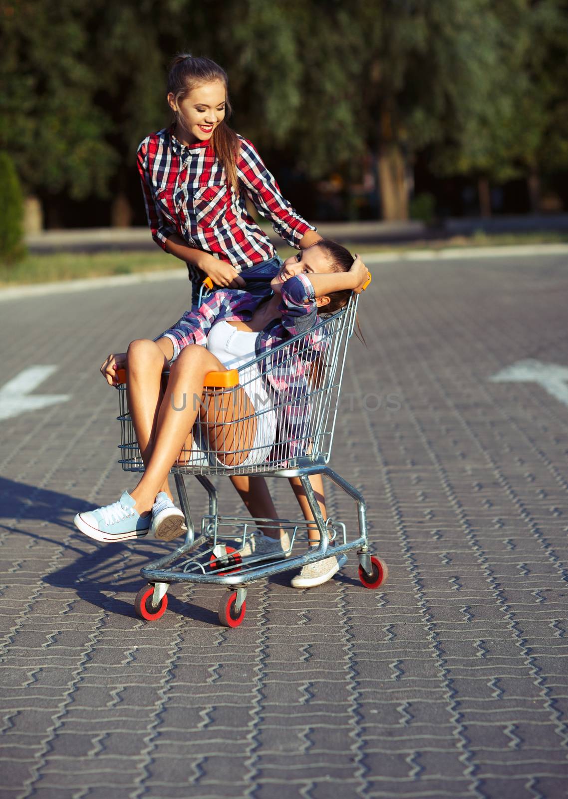 Two happy beautiful teen girls driving shopping cart outdoors, lifestyle concept