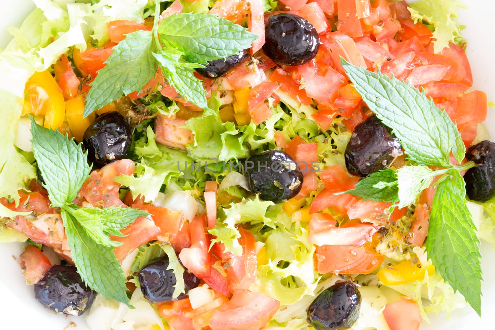 Fresh plain Mediterranean salad with olives, lettuce, tomato and colorful bell peppers garnished with sprigs of fresh mint, close up view from above