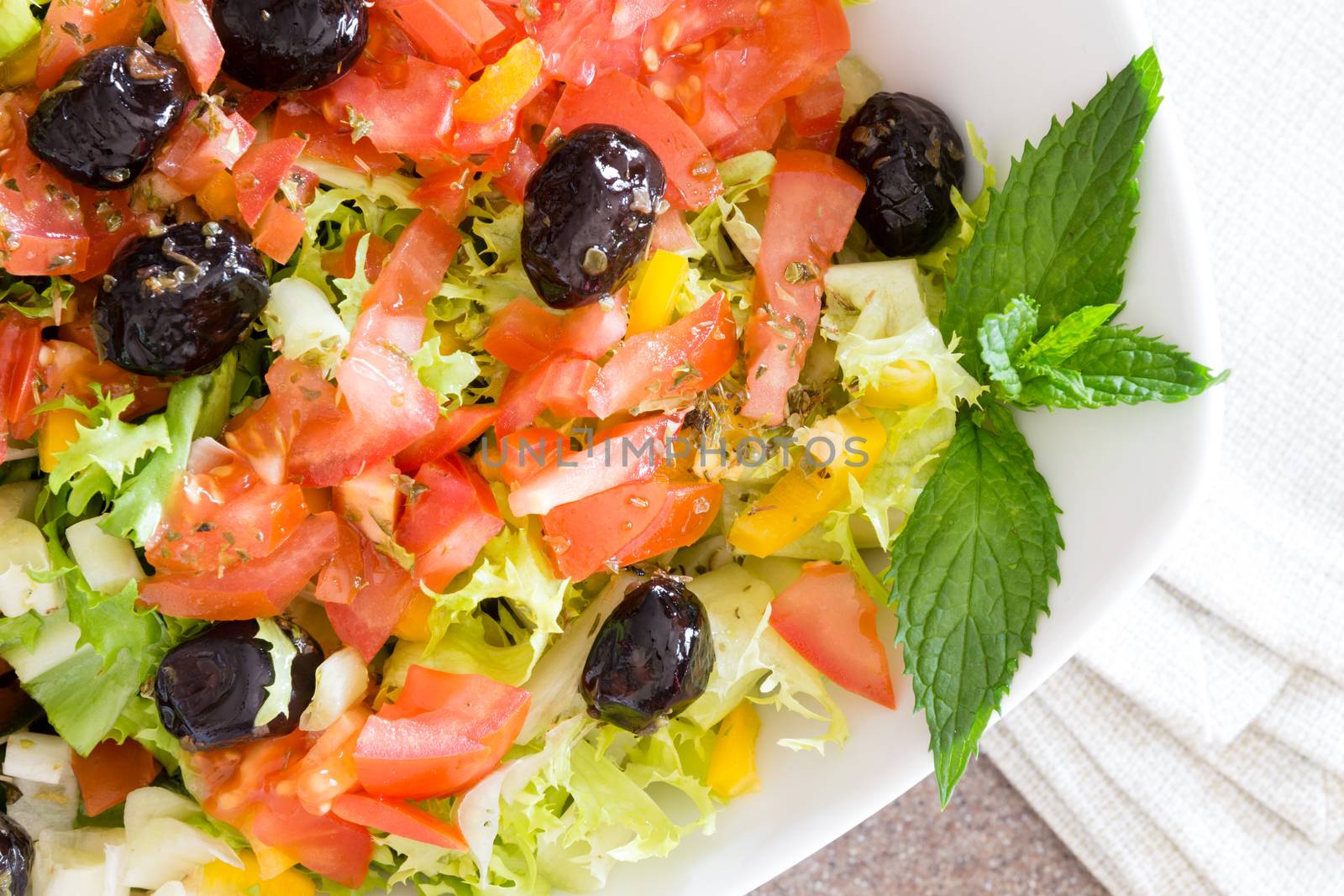 Healthy farm fresh Mediterranean salad with black olives, lettuce, tomato and sweet bell peppers garnished with sprigs of mint for flavoring, close up detail