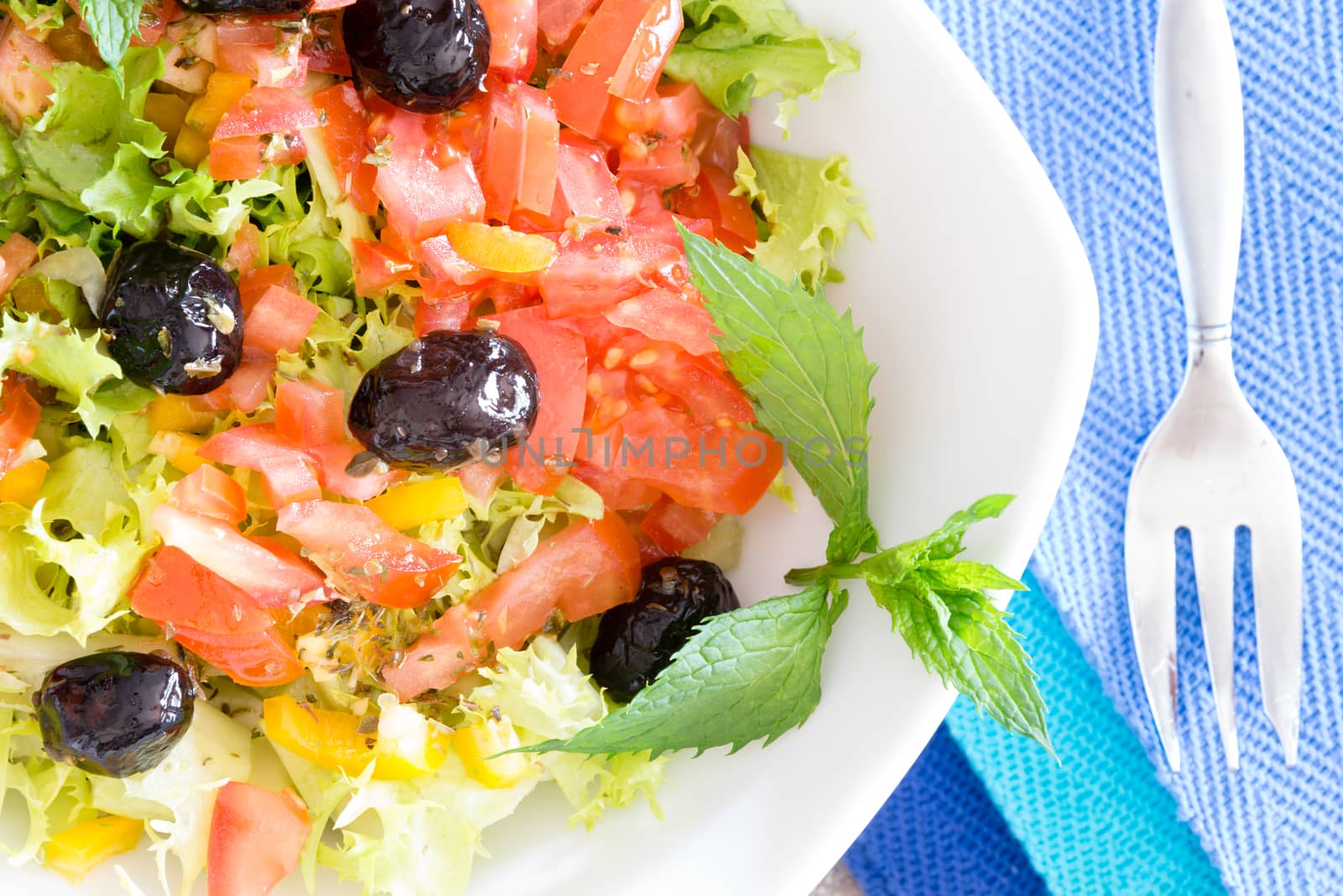 Healthy mixed leafy green salad garnished with black olives and sprigs of aromatic mint served on blue napkins for a tasty appetizer or accompaniment