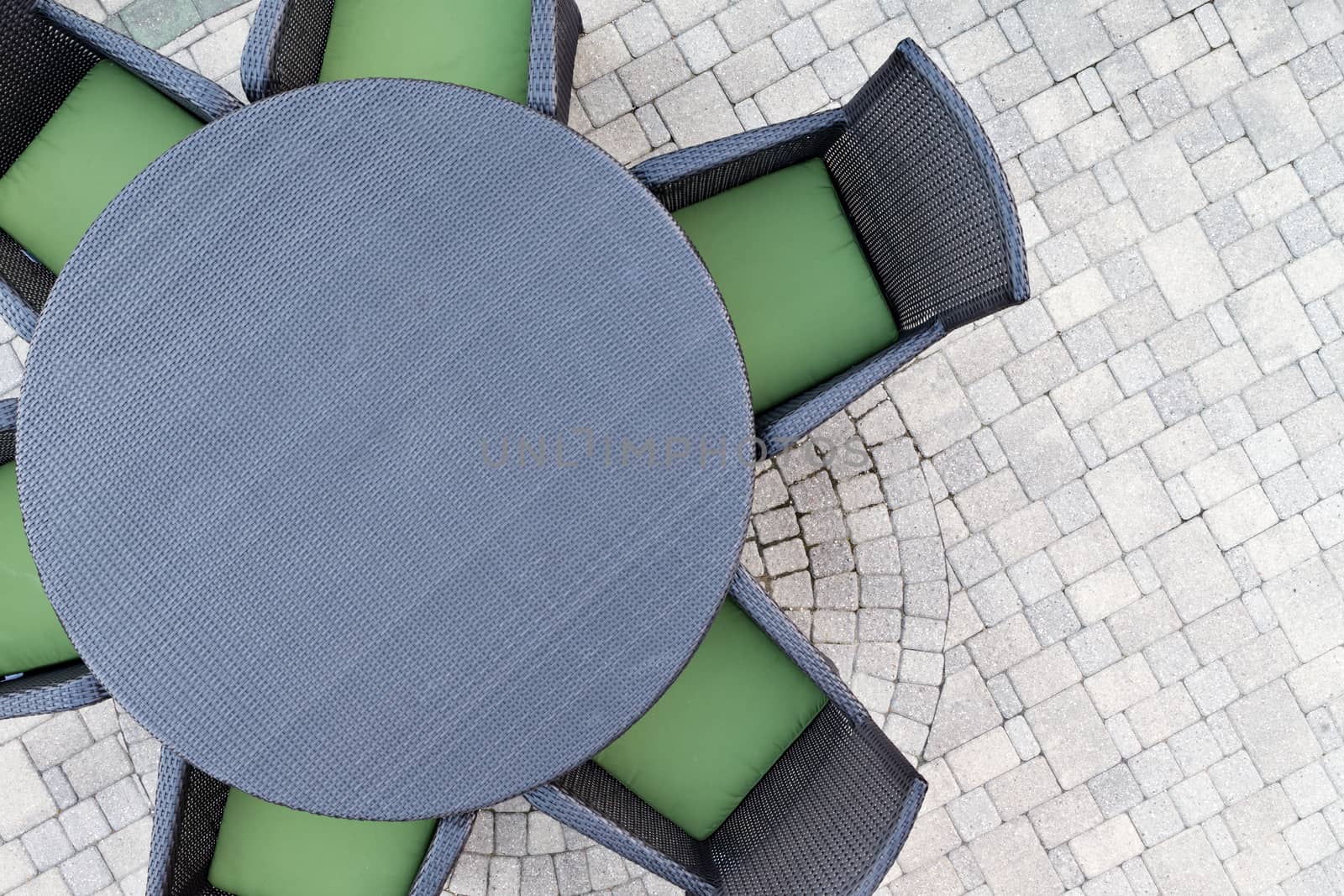 Six seater outdoor patio set with comfortable green cushions and a round dining table on a brick paved open-air patio with copyspace, overhead view