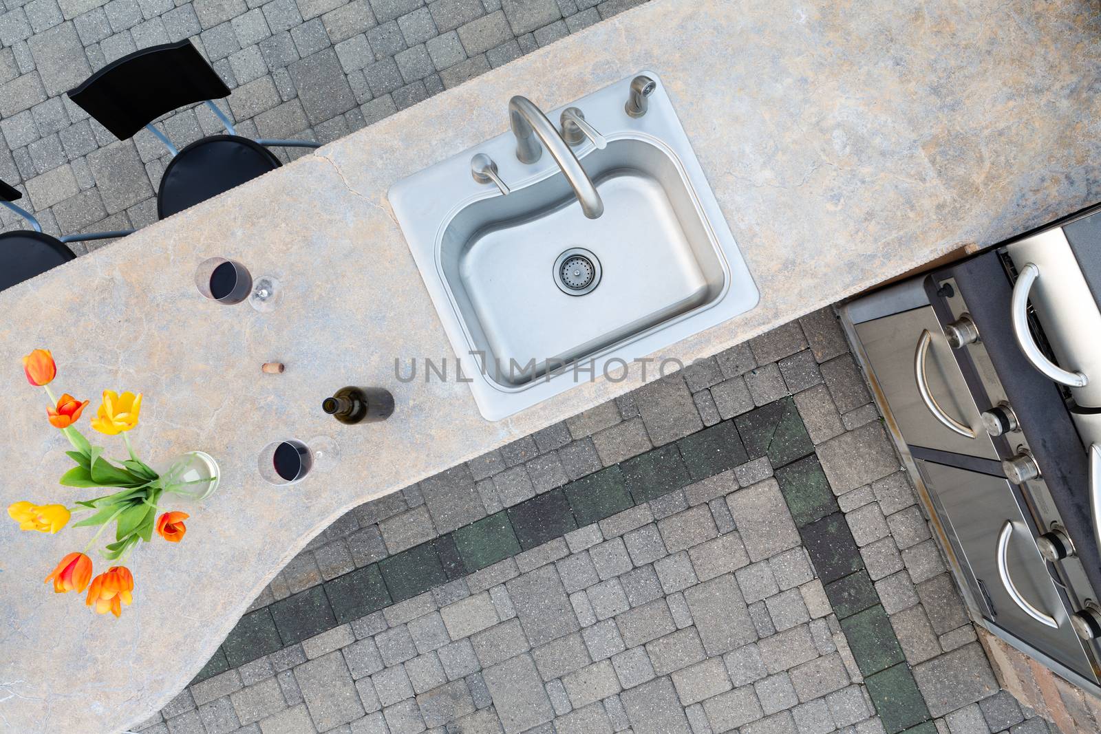 Exotic concrete counter top and sink in an outdoor kitchen set with two glasses and a bottle of red wine and a vase of tulips alongside a built in gas barbecue for healthy outdoor living