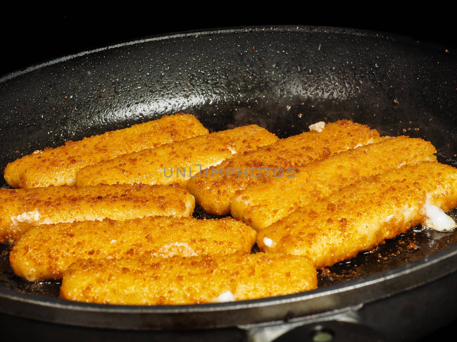 Closeup of crispy breaded fish fingers in hot fry pan by Arvebettum