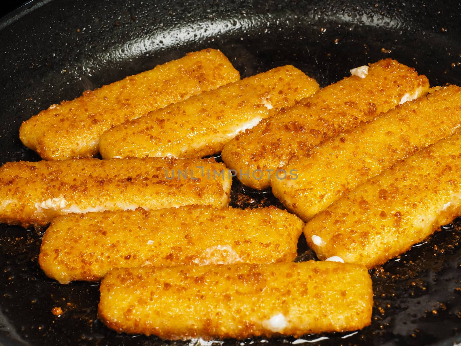 Closeup of crispy breaded fish fingers in hot fry pan by Arvebettum