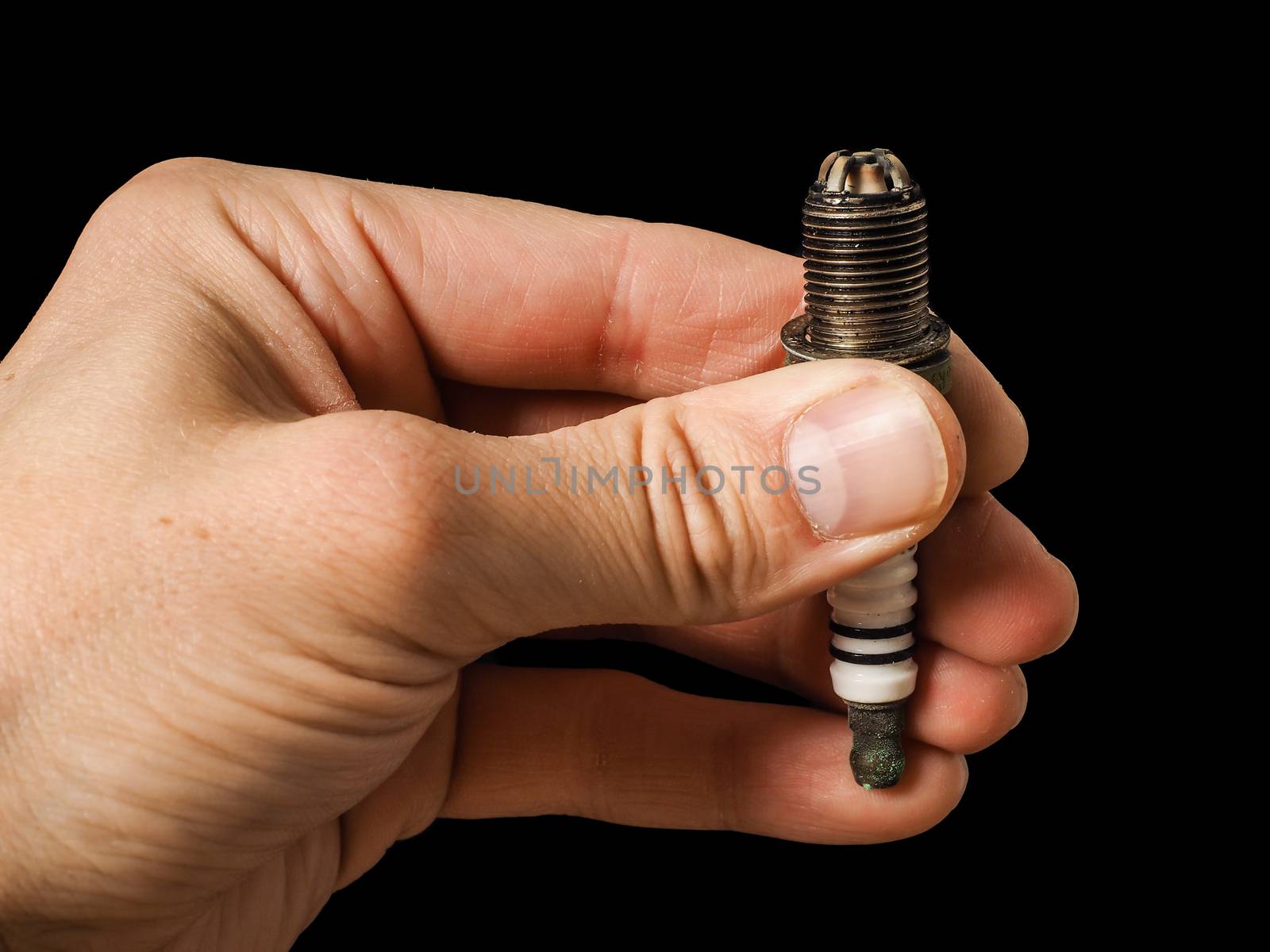 Closeup of a worn spark plug held by caucasian male fingers by Arvebettum