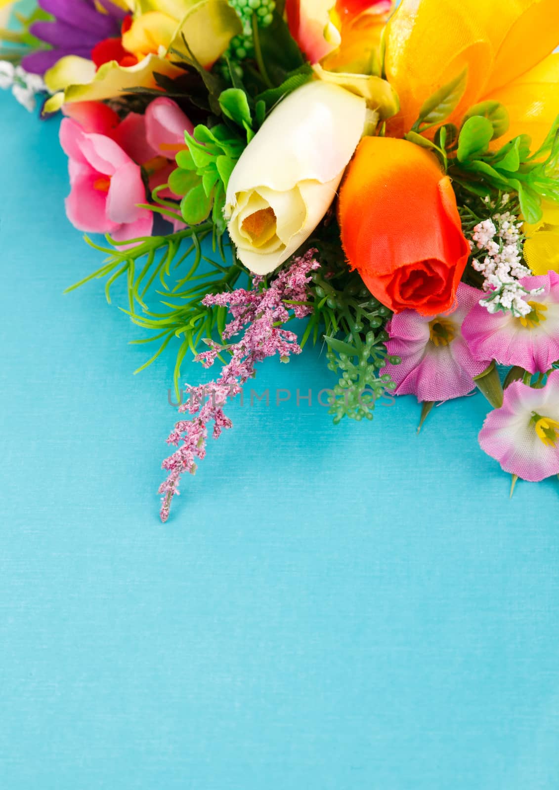 artificial flowers on blue background with place for label