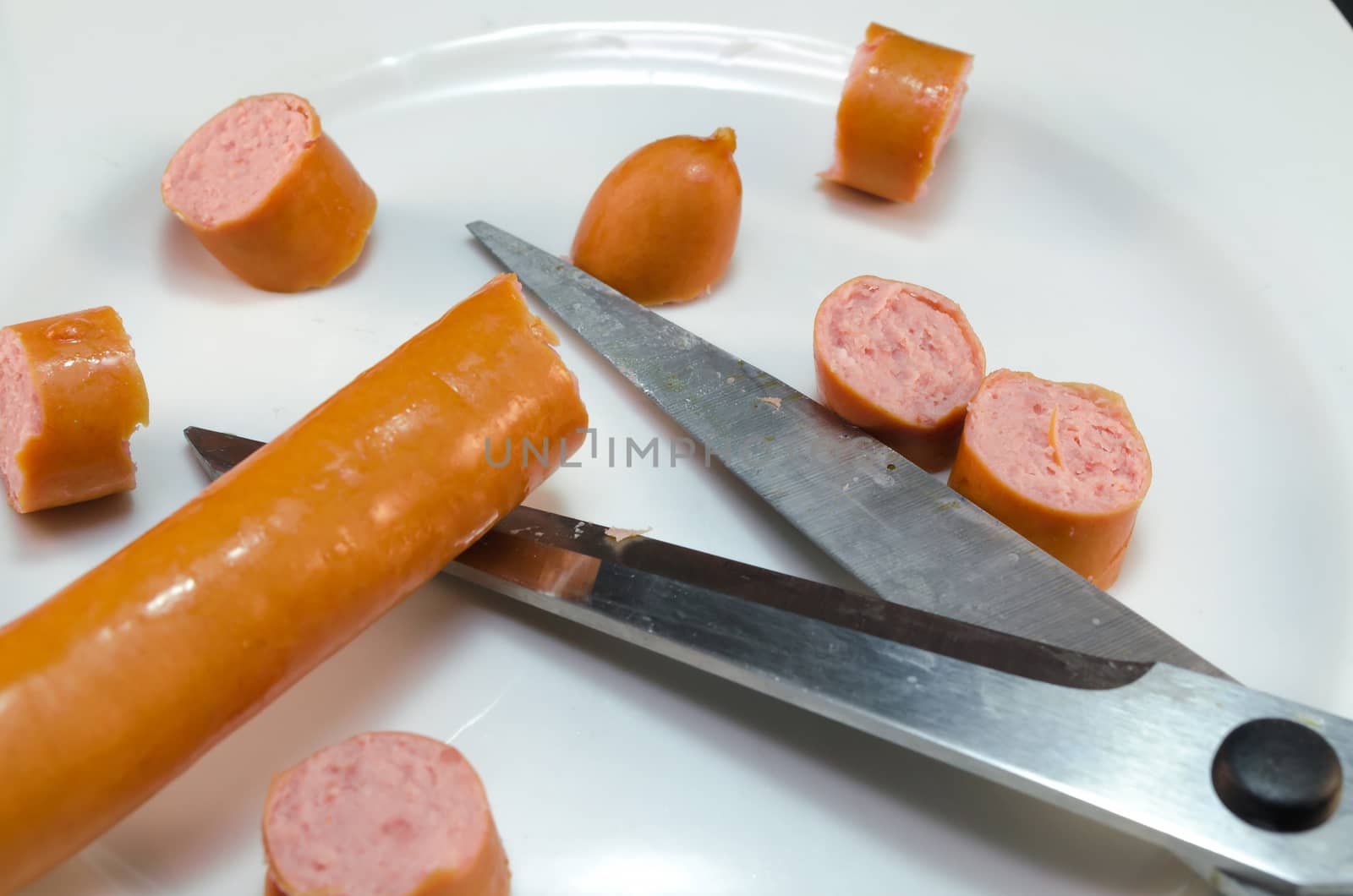 Cut Frankfurter sausages with scissors.
Sausage pieces on white plate.