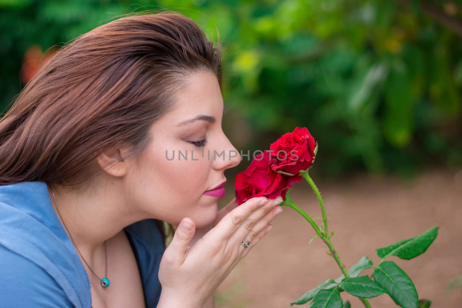 Young beautiful Caucasian girl smelling the roses in the garden.