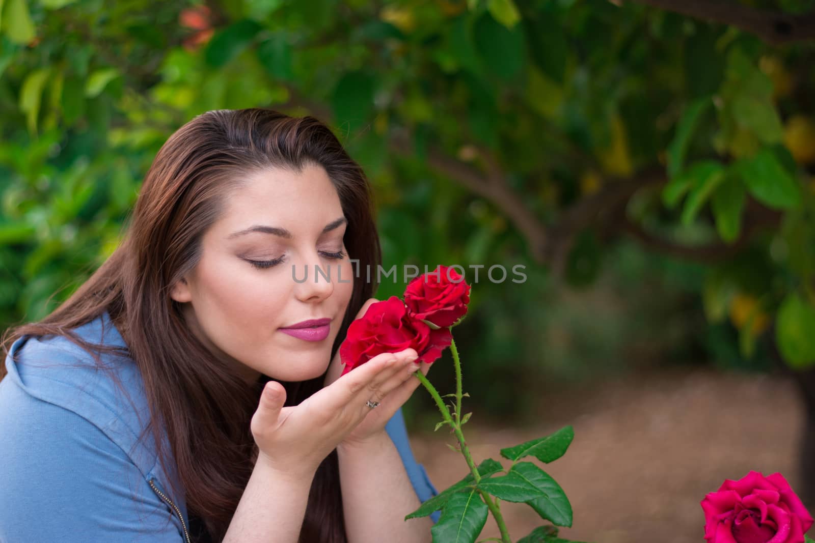 Young beautiful Caucasian girl smelling the roses in the garden.