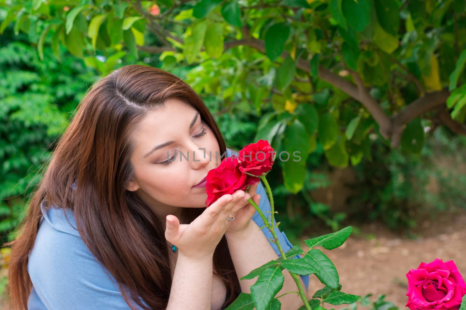 Young beautiful Caucasian girl smelling the roses in the garden.