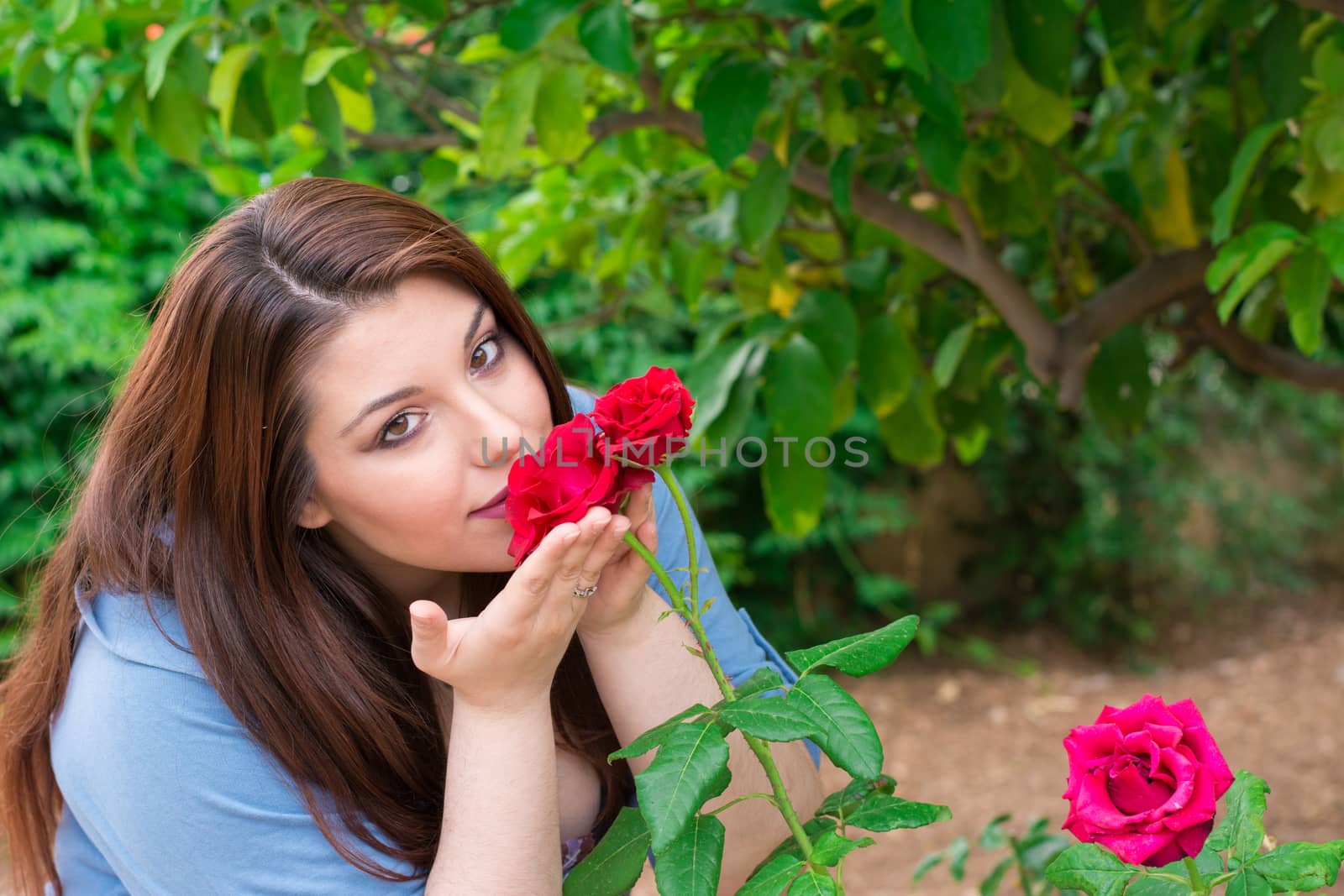 Young beautiful Caucasian girl smelling the roses in the garden.
