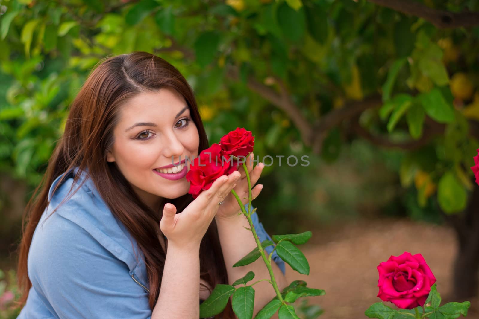 Young beautiful Caucasian girl smelling the roses in the garden.