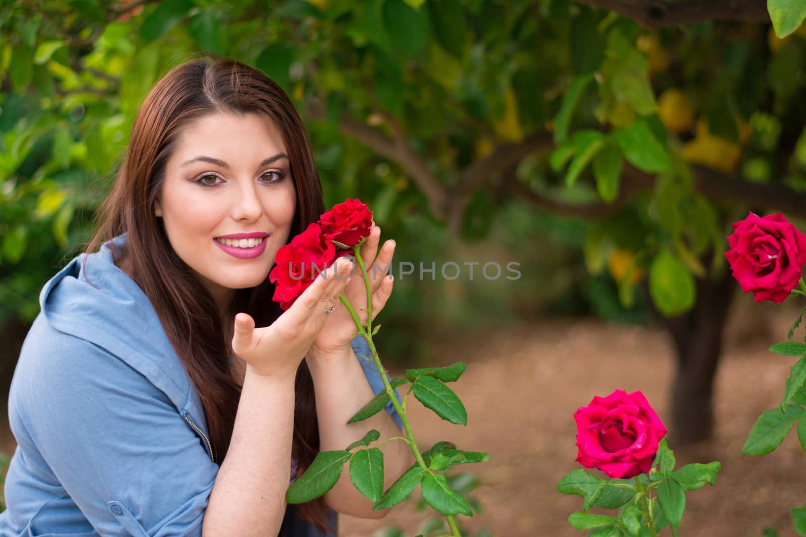 Young beautiful caucasian girl holding red roses in the garden, smiling.