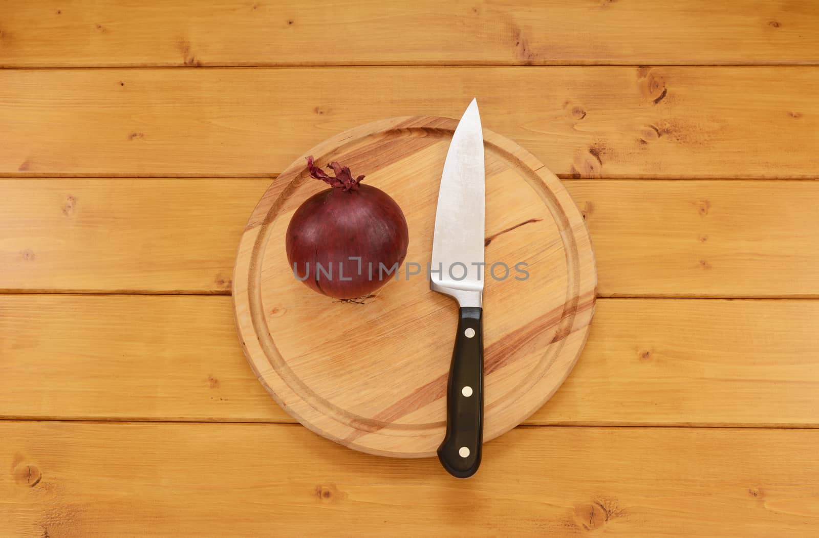 Whole raw red onion with a sharp kitchen knife on a wooden chopping board