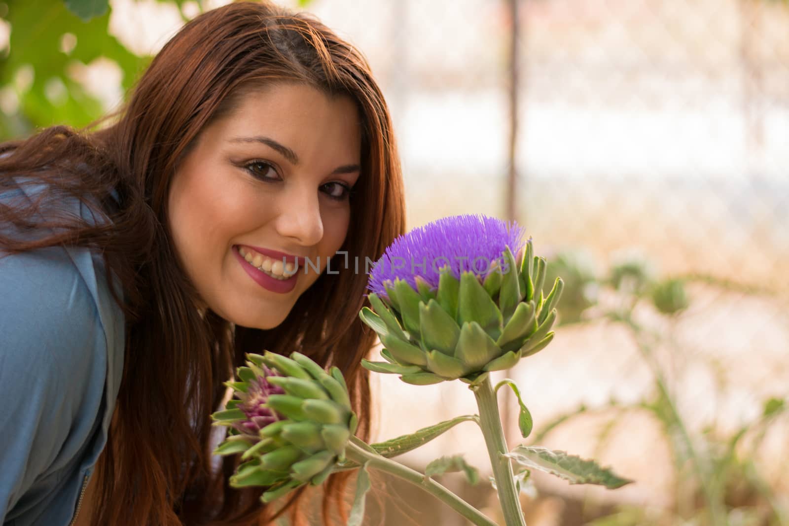 Young beautiful caucasian girl smelling a big artichoke flower.