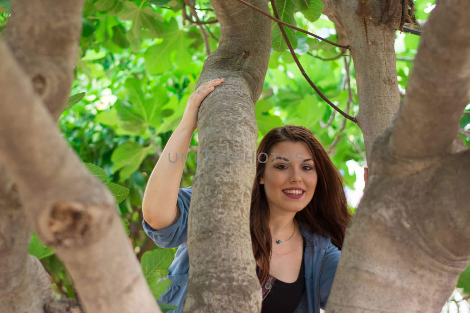 Young beautiful caucasian girl smiling behind a fig tree.