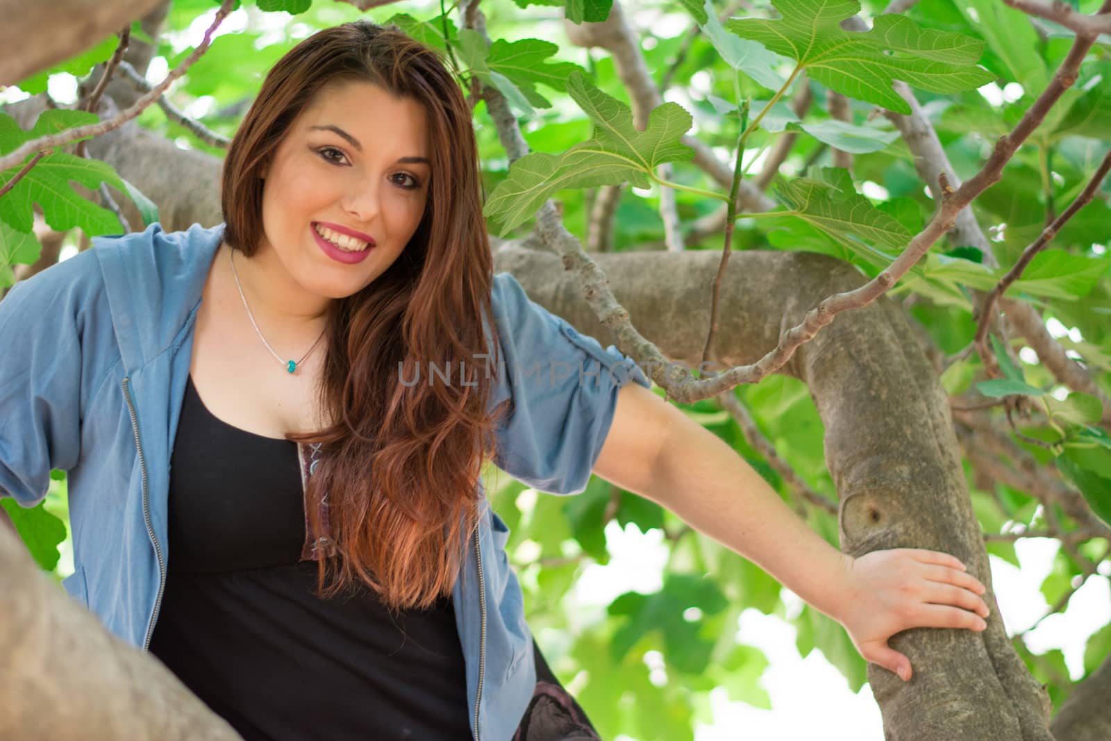 Young beautiful caucasian girl smiling while being on a big fig tree.