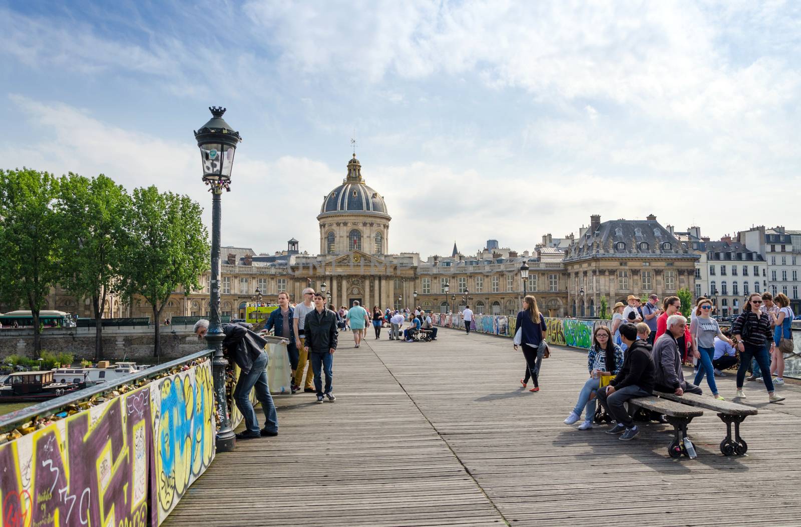 Paris, France - May 13, 2015: People visit Institut de France and the Pont des Arts or Passerelle des Arts bridge across river Seine in Paris, France. on May 13, 2015.