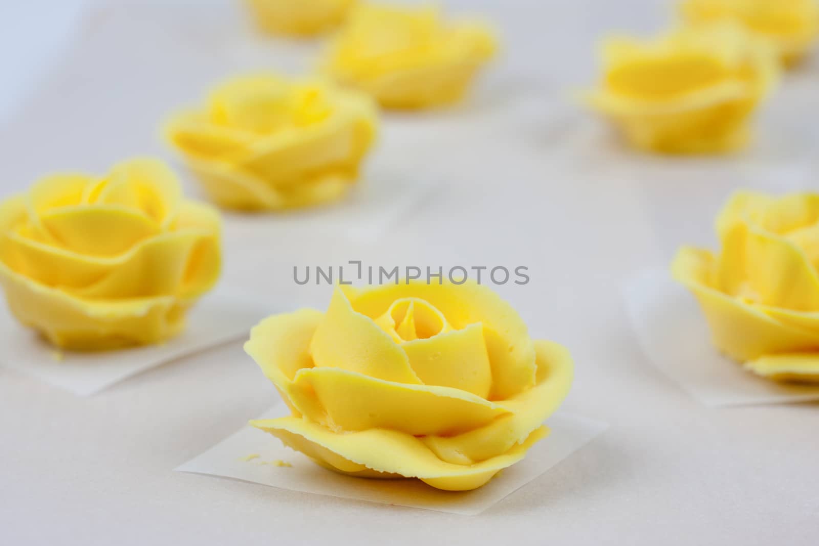 Yellow roses made from butter cream icing, drying on parchment paper.
