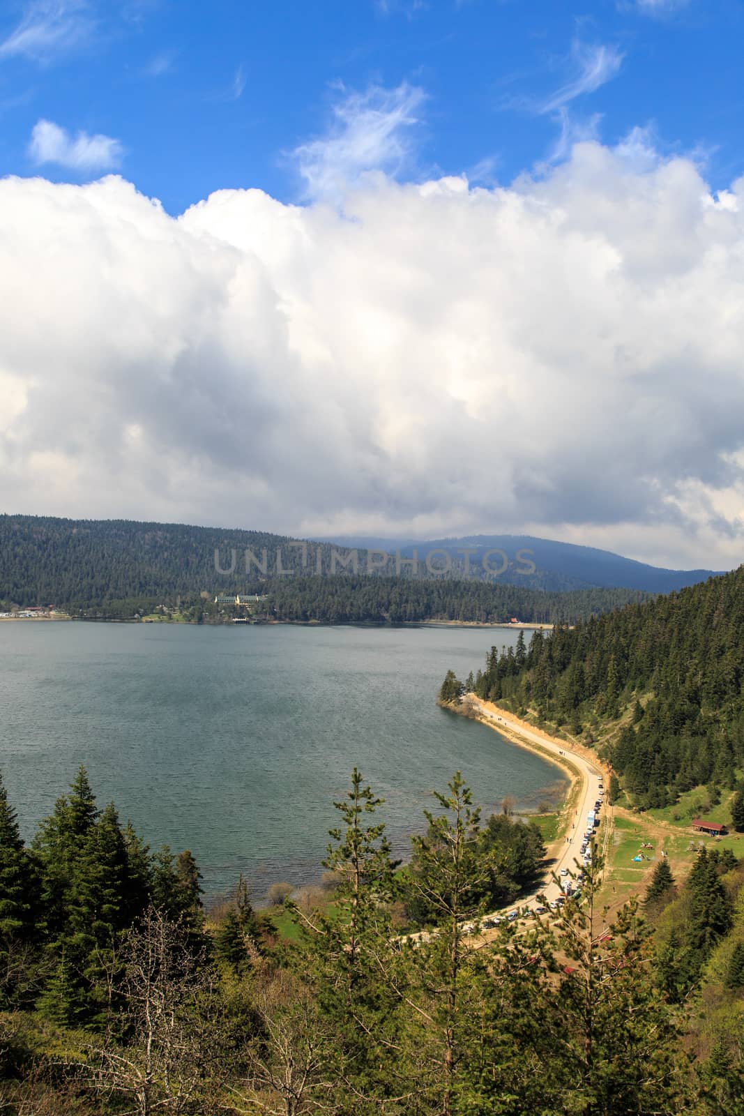 Lake or river landscape with trees and mountains around, under cloudy sky.