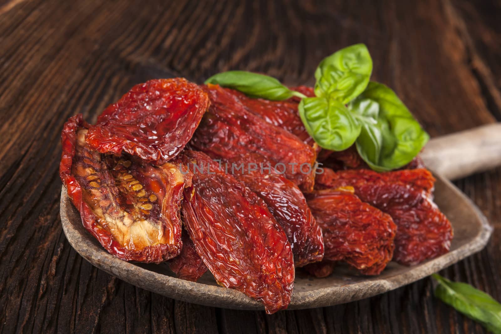 Sundried tomatoes and fresh basil leaves on brown wooden background. Culinary italian eating. 