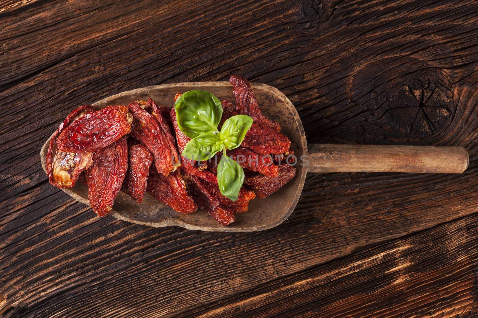 Sundried tomatoes and fresh basil leaves on brown wooden background. Culinary italian eating. 