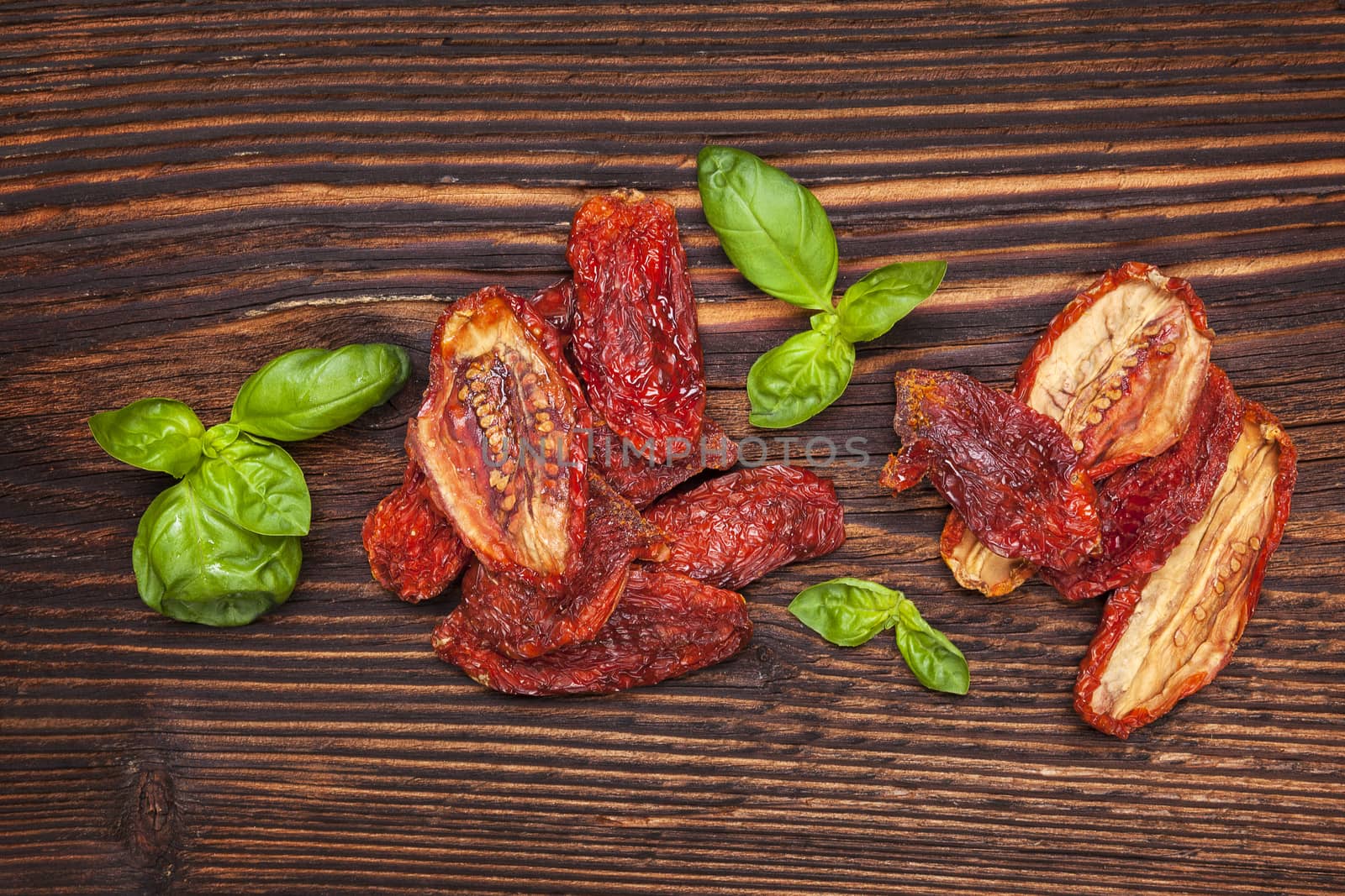 Dry tomatoes and fresh basil leaves on brown wooden background, top view. Italian eating, rustic styles.