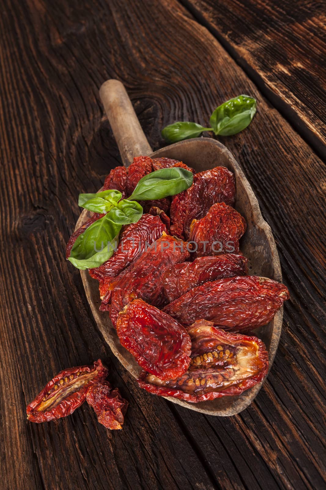 Sundried tomatoes and fresh basil leaves on brown wooden background. Culinary italian eating. 