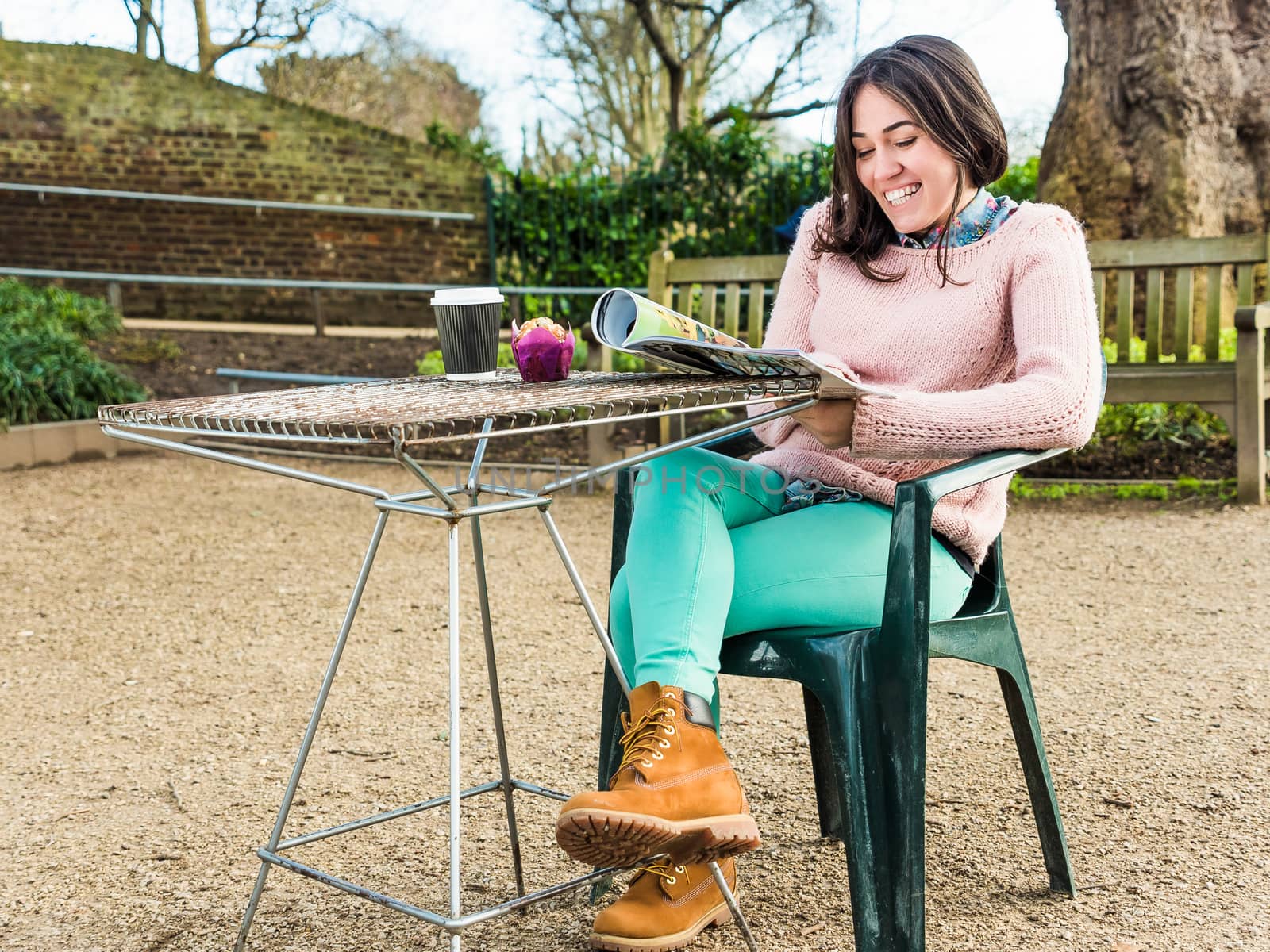 Attractive Young Woman Reads a Magazine Sitting in a Cafe Outside