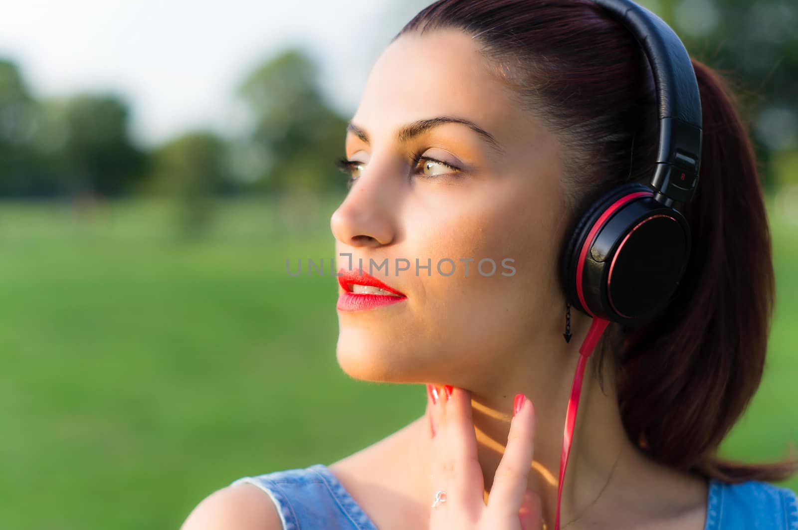 Beautiful Young Woman Listening Music Through Headphones in a Park