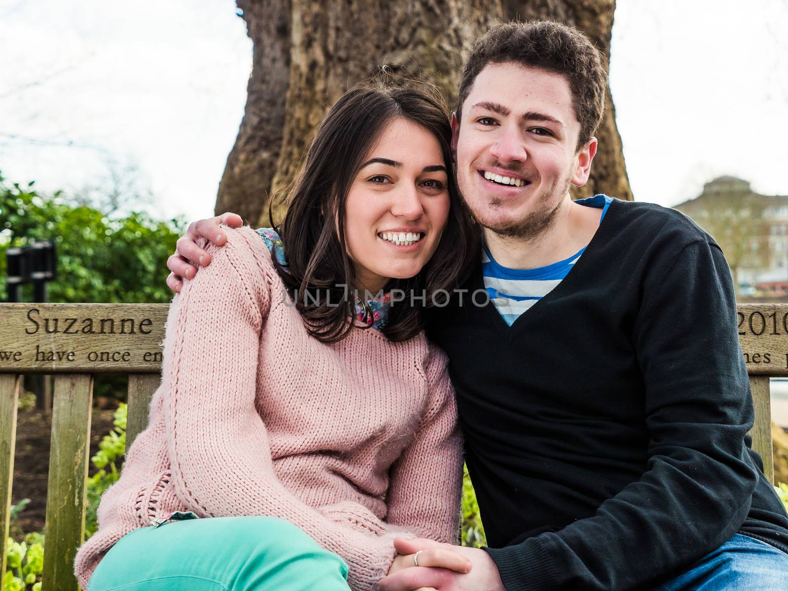 Romantic Young Couple Sitting On Park Bench Together and Smiling Looking at the Camera