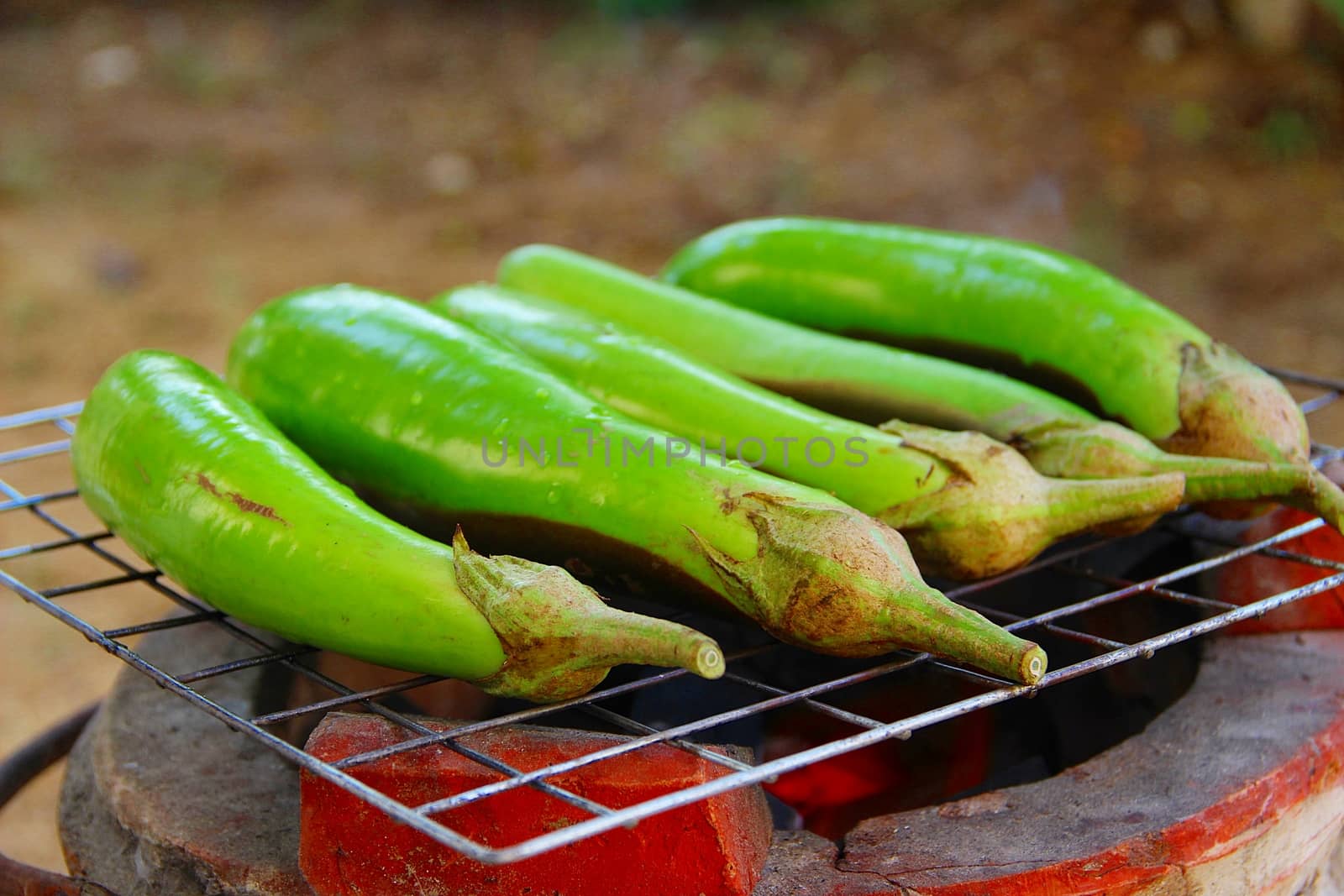 Grilling eggplants on earthen stove, old style Asian cooking
