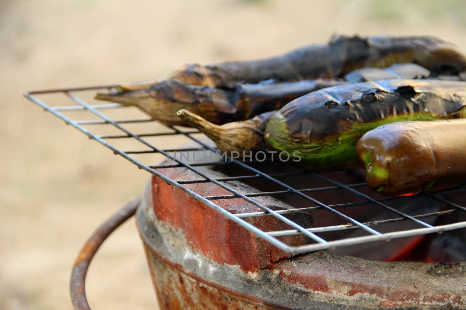 Grilling eggplants on earthen stove, old style Asian cooking