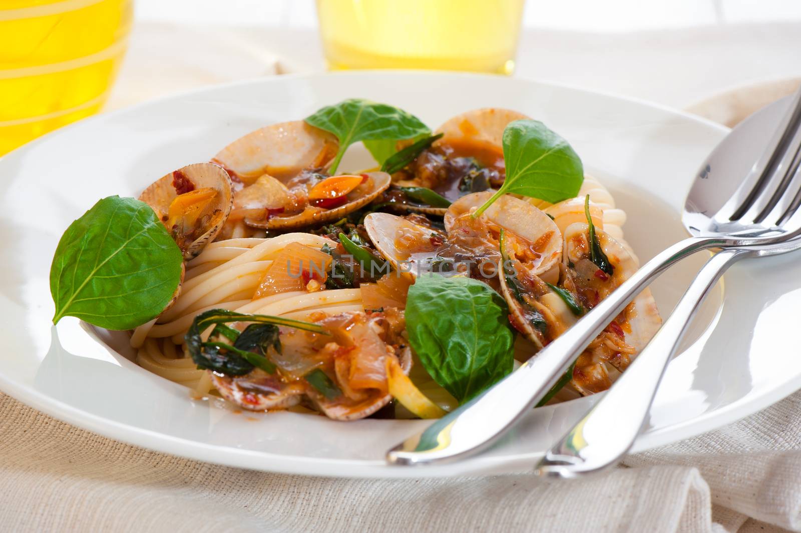 A white plate with delicious spaghetti shellfish and green basil. A glass of white wine in background.