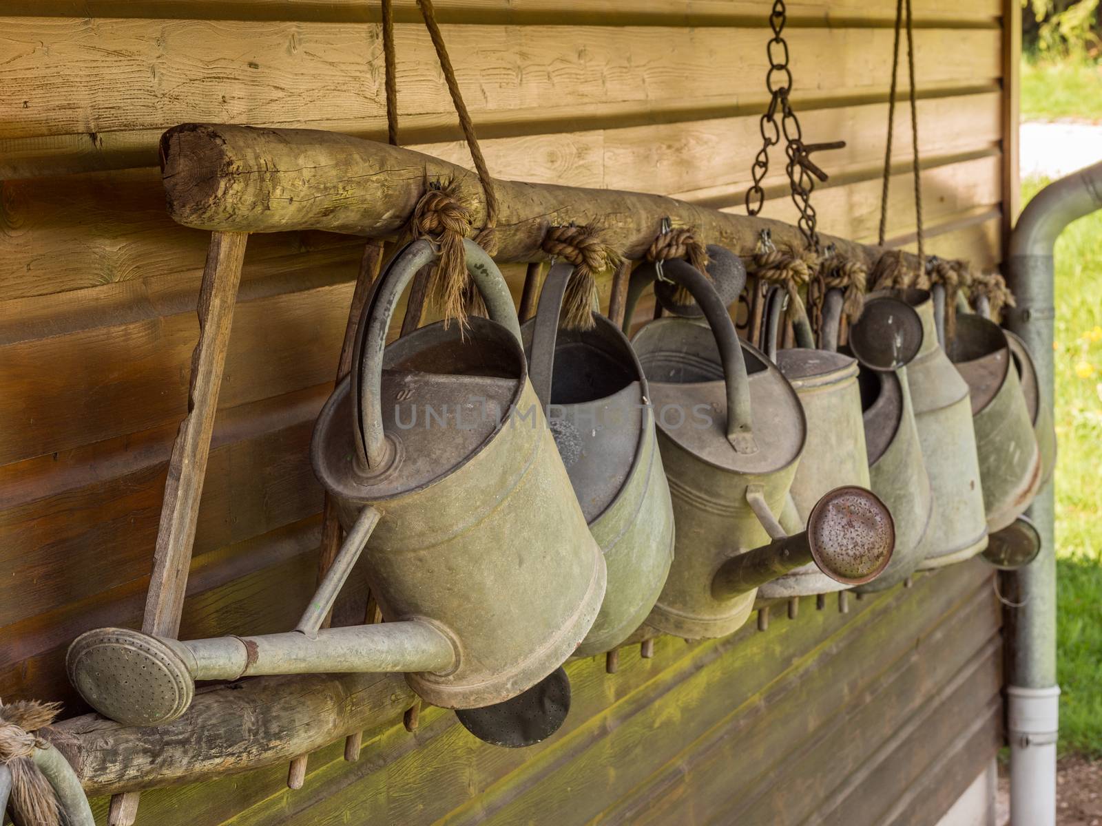 A row of metal watering cans hanging in front of a wooden wall