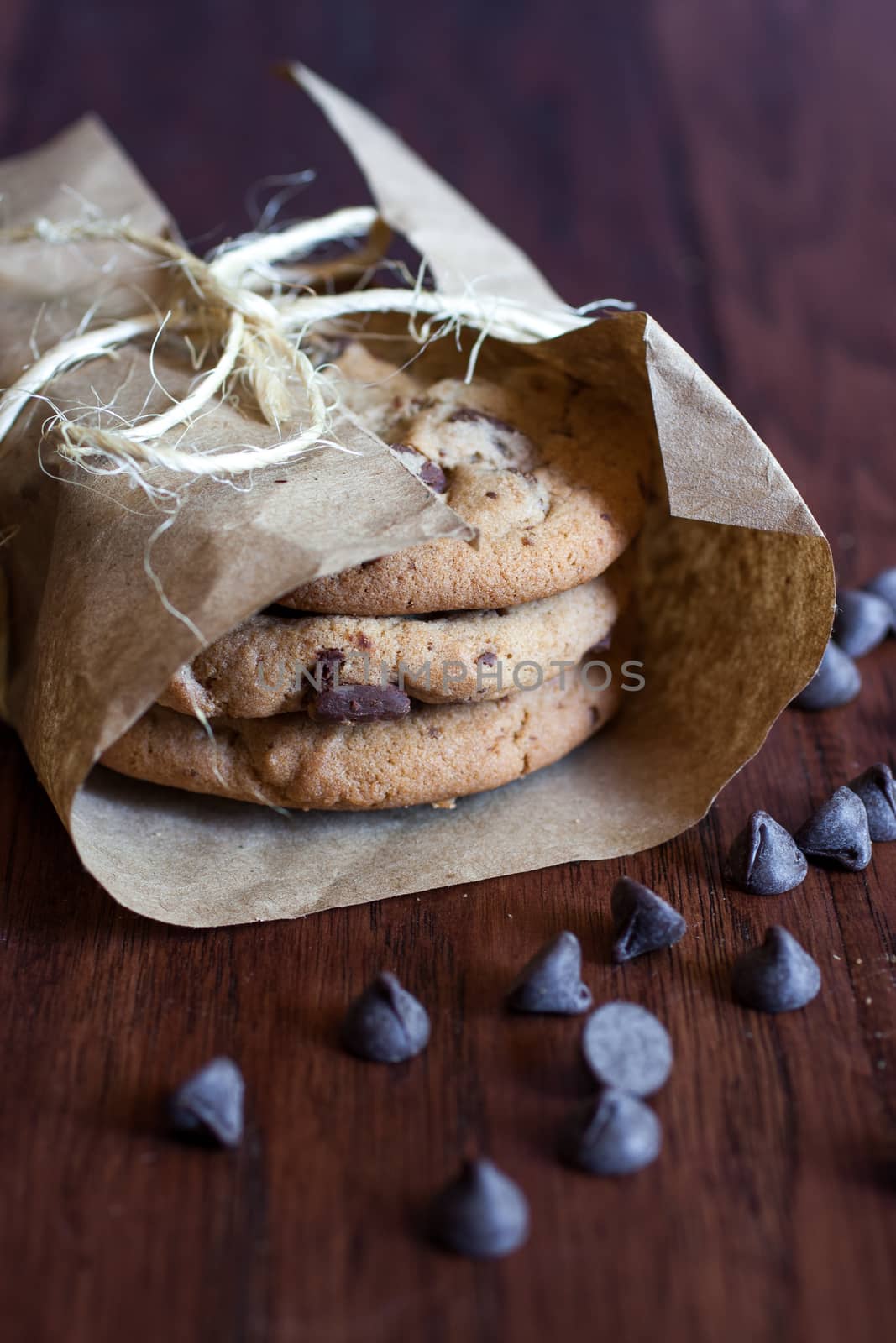 Fresh chocolate chunk cookies wrapped in paper and tied up with twine and sitting on a wooden counter.
