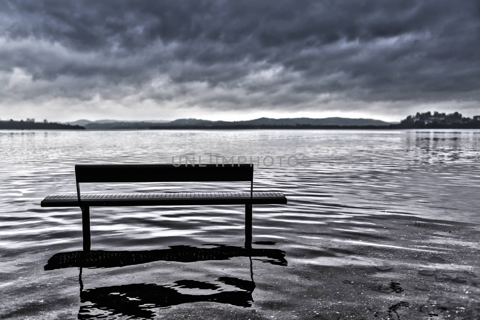 bench on Lake Varese overflows in autumn season with cloudy sky, Lombardy - Italy