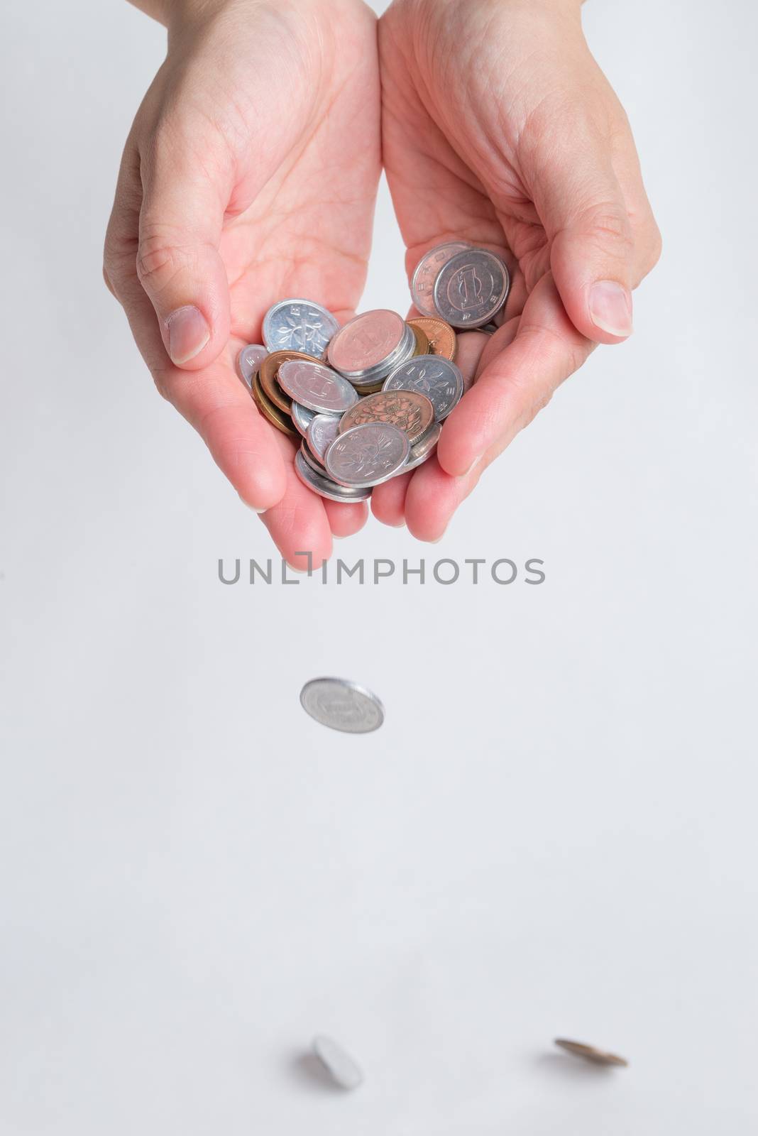 A woman's hands cupped holding many various Japanese Yen coins dropping a few on a white background.