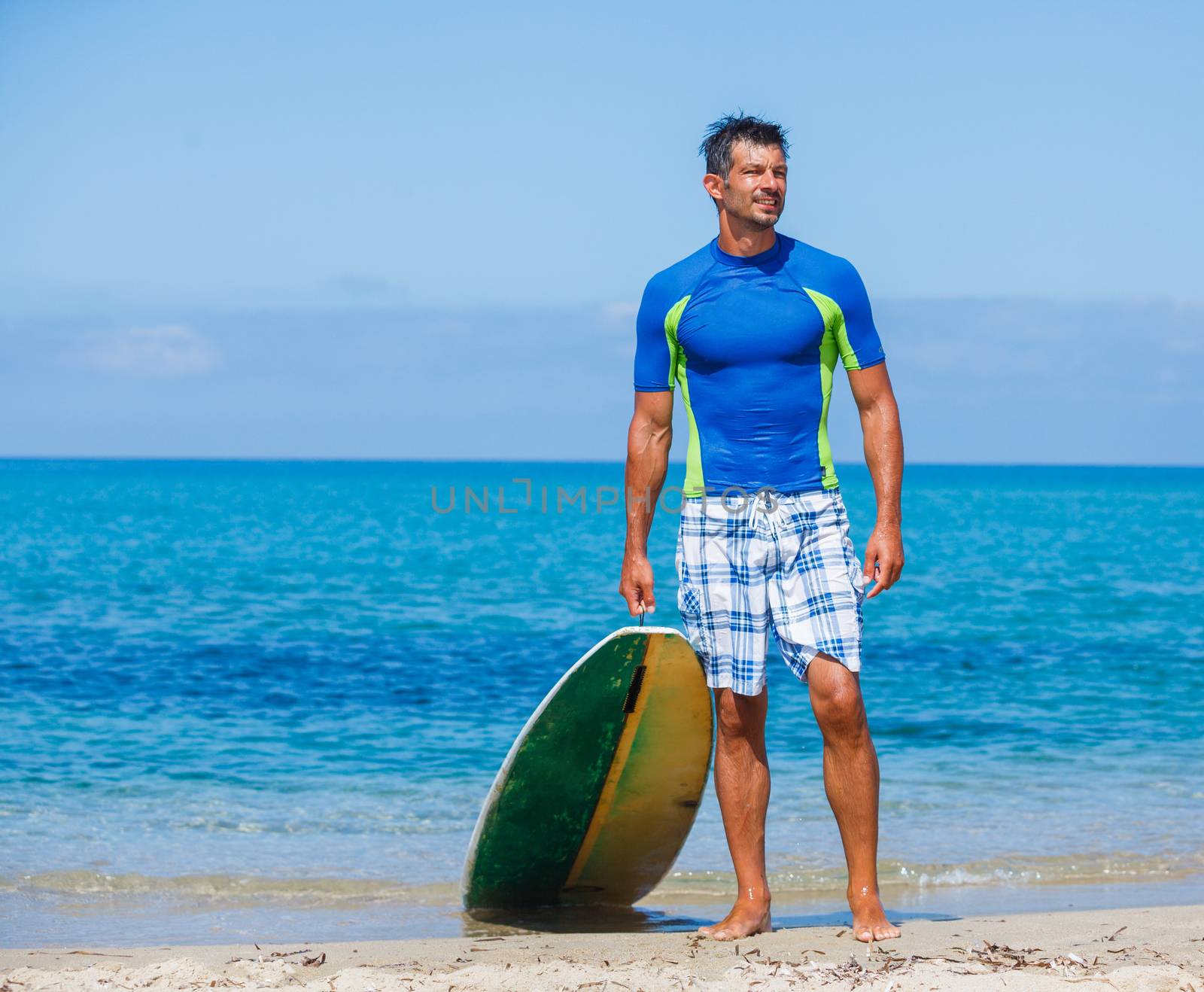 Strong young surf man at the beach with a surfboard.