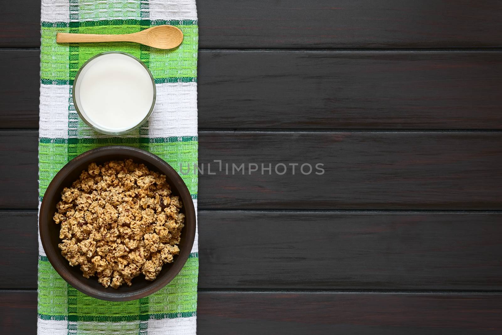 Dried berry and oatmeal breakfast cereal in rustic bowl with a glass of milk, photographed overhead on dark wood with natural light 