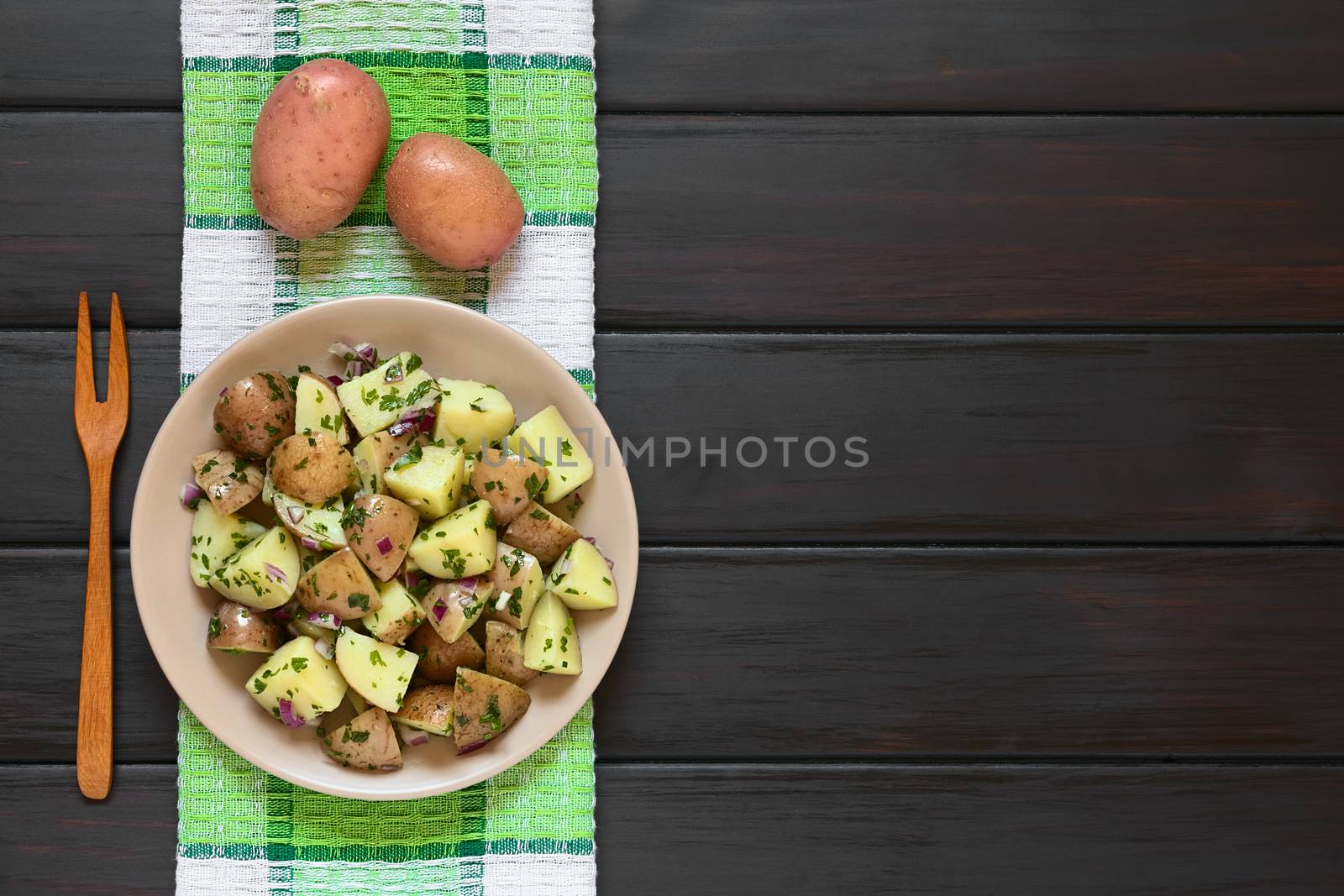 Salad of jacket potato, red onion and herbs served on plate, photographed overhead on dark wood with natural light