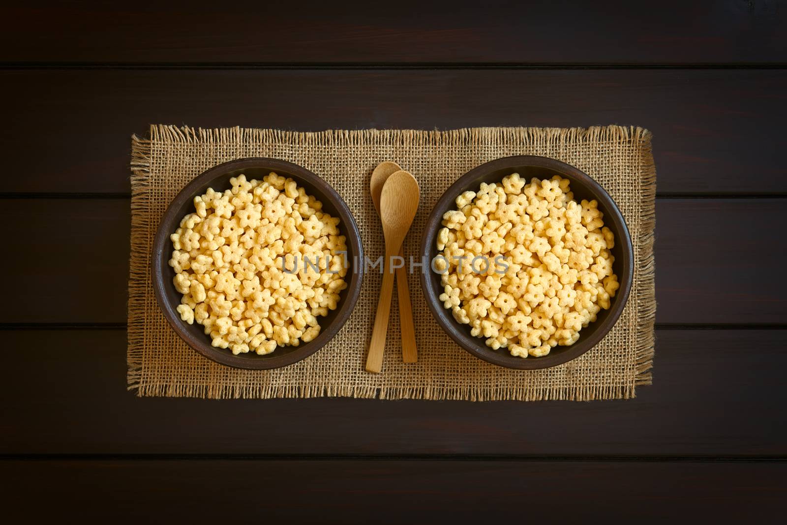 Honey flavored breakfast cereal in rustic bowls with small wooden spoons, photographed overhead on dark wood with natural light 