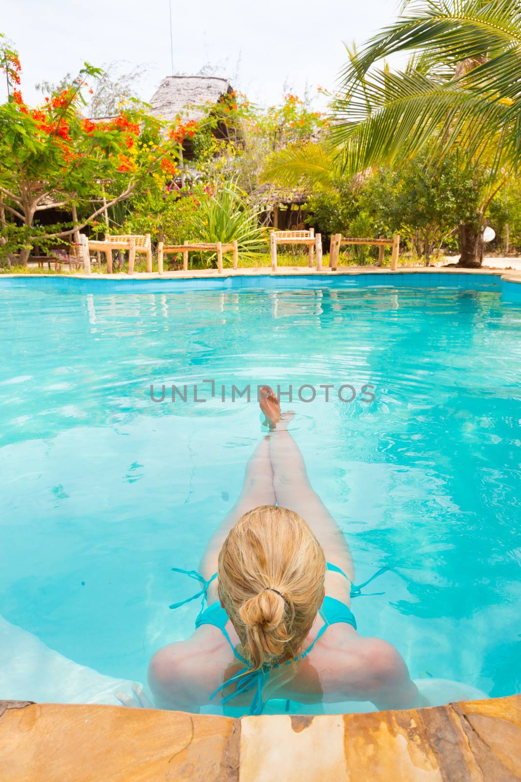 Beautiful Caucasian woman floating in turquoise blue swimming pool.