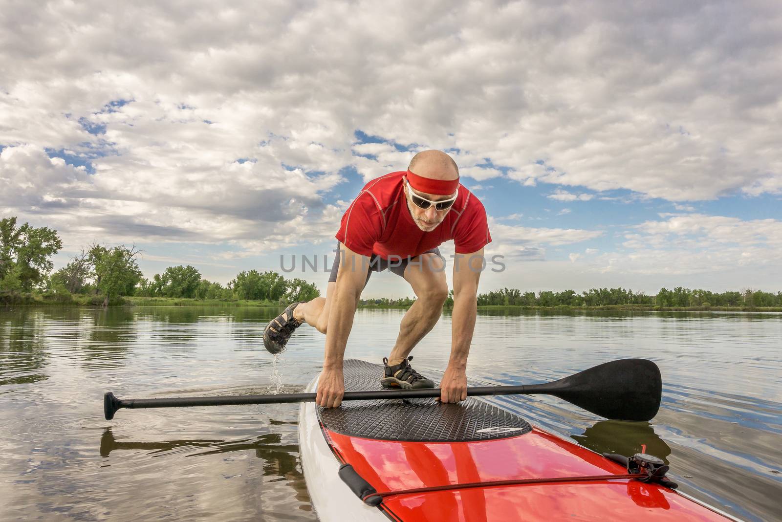 senior male paddler starting his workout on a  stand up paddleboard -  a local lake in Colorado under cloudy sky