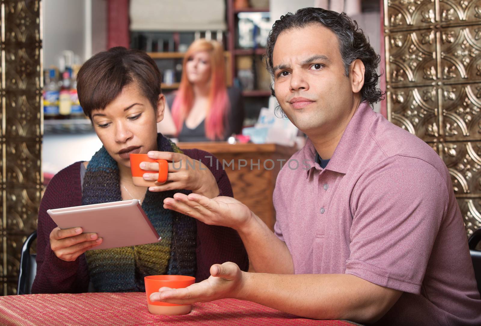 Annoyed spouse sitting with wife reading tablet computer