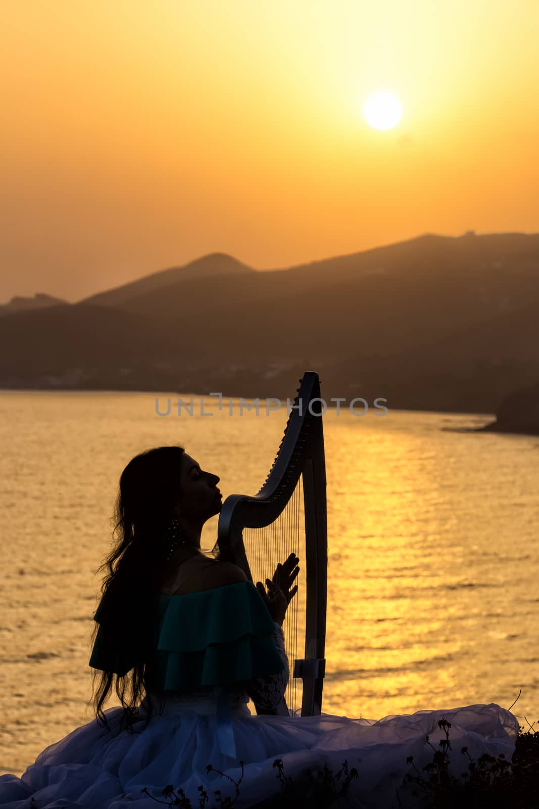 Silhouette woman plays harp by the sea at sunset in Santorini, Greece