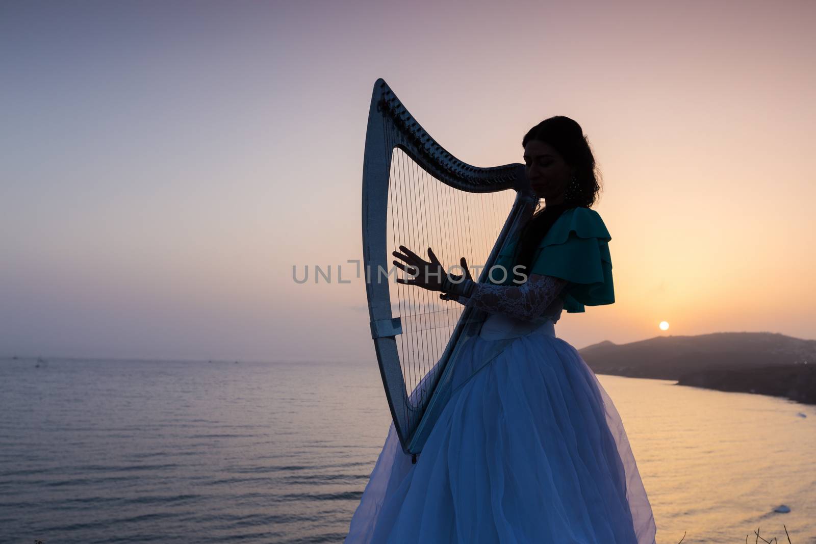 Silhouette woman plays harp by the sea at sunset in Santorini, Greece
