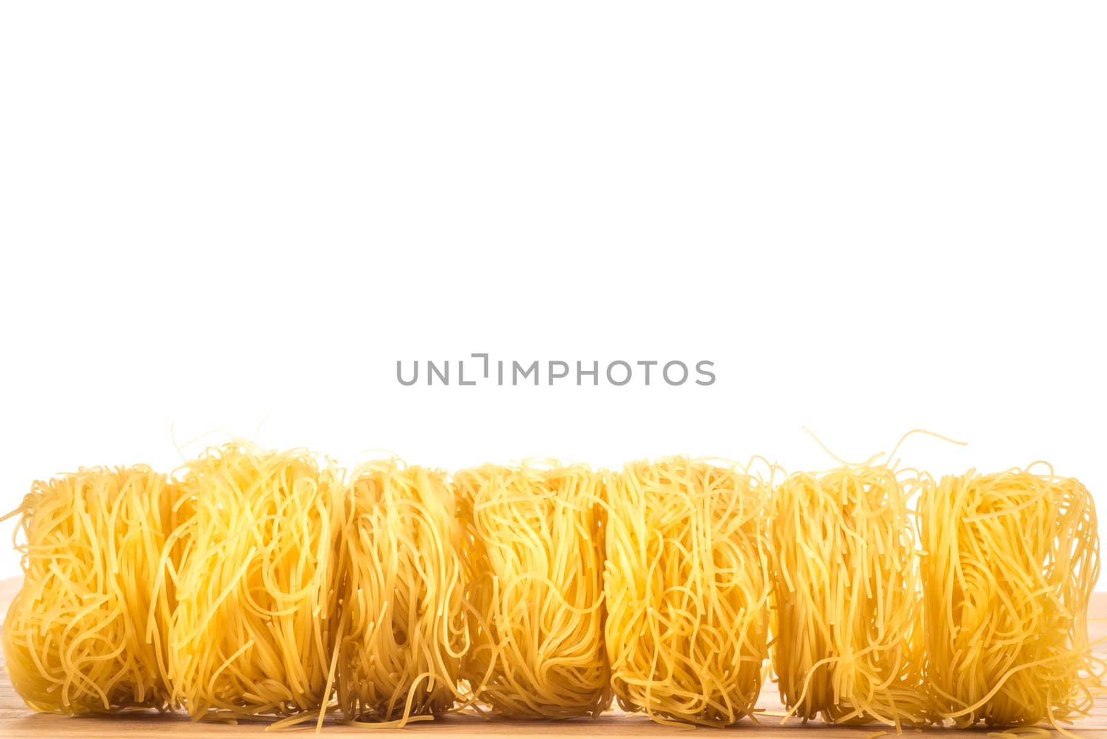 Seven rolls of Angel's Hair Spaghetti lie next to each other on a wooden surface to create a line with much white background above.