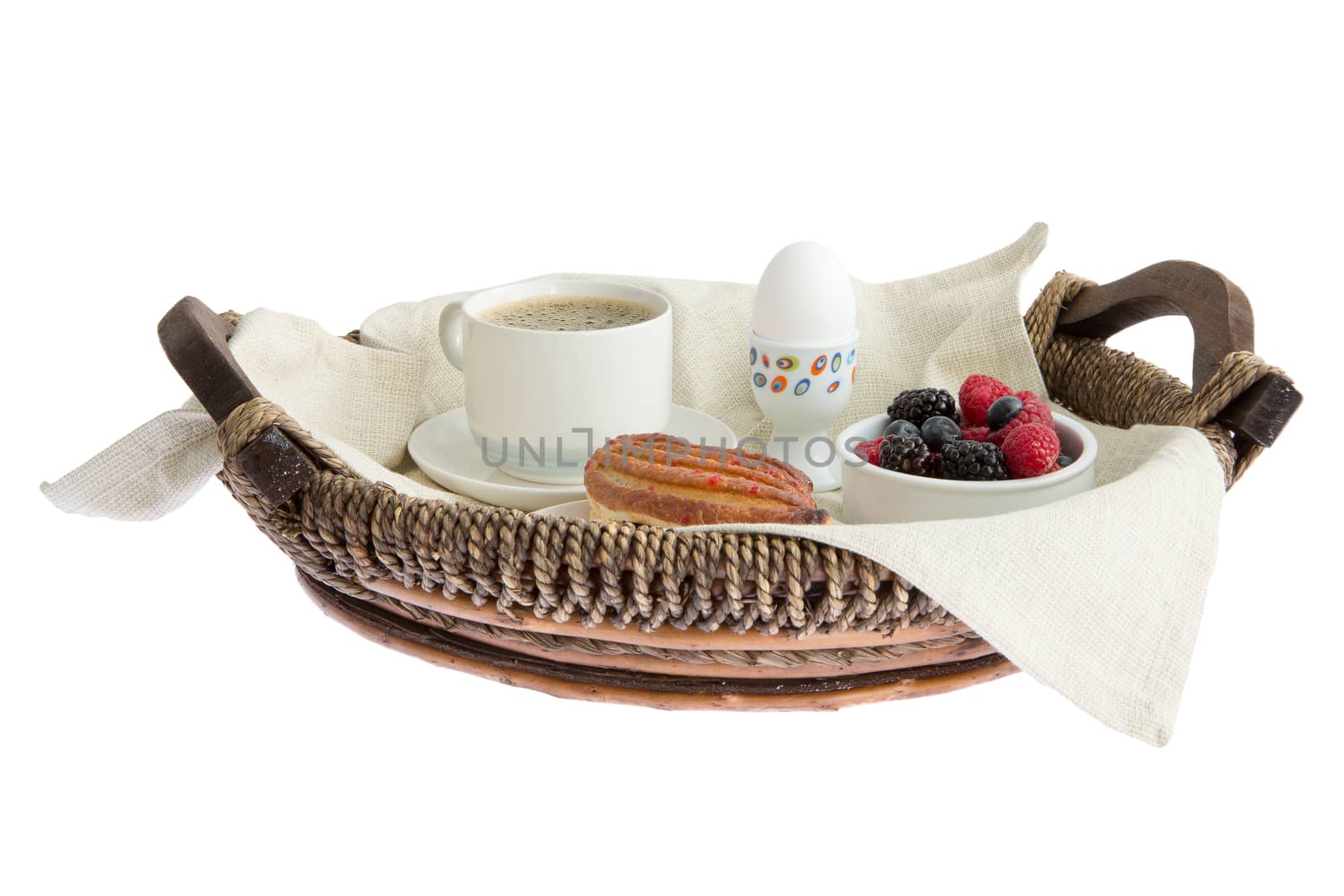 Rustic wickerwork breakfast tray set with coffee, egg, pastry and fresh assorted berries viewed low angle isolated on white
